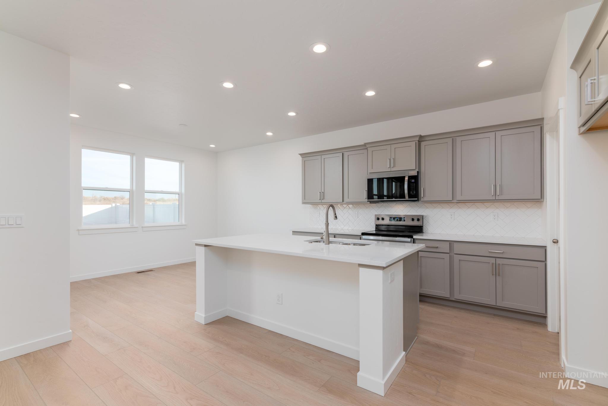 Kitchen with tasteful backsplash, appliances with stainless steel finishes, recessed lighting, a center island with sink, and light wood-style floors