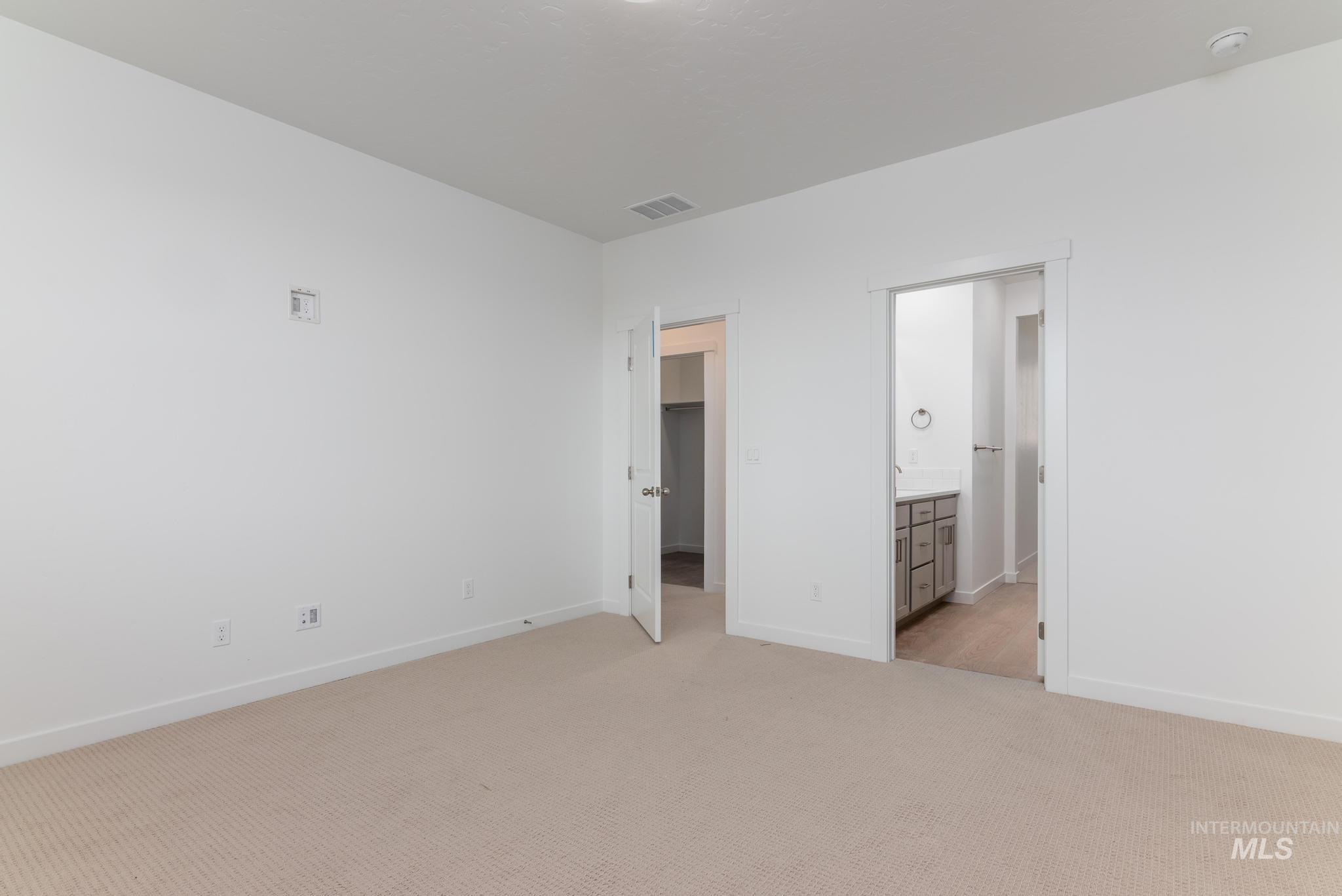 Unfurnished bedroom with a walk in closet, light carpet, and ensuite bath