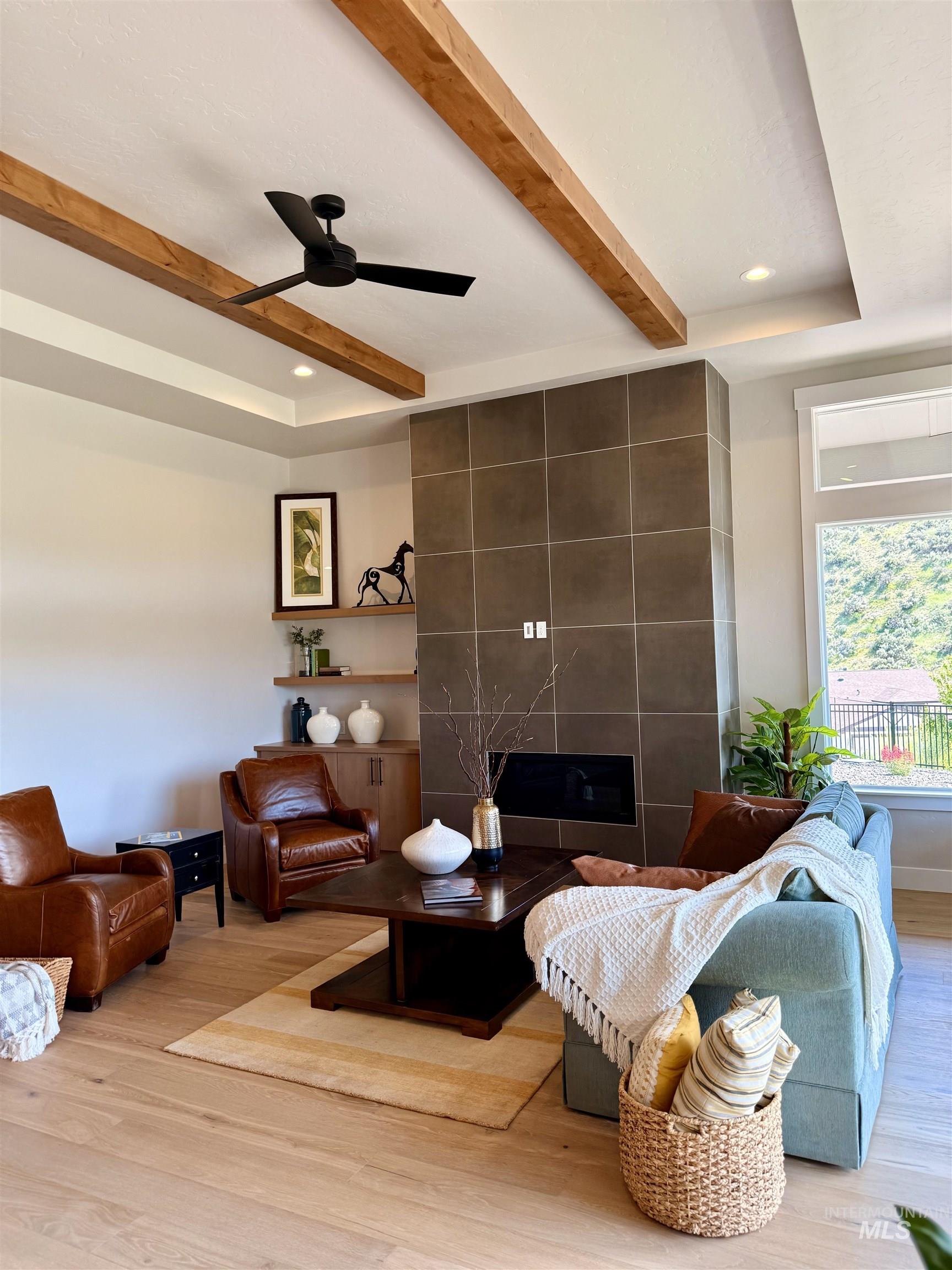 Living room with beamed ceiling, a tiled fireplace, light wood finished floors, a ceiling fan, and recessed lighting