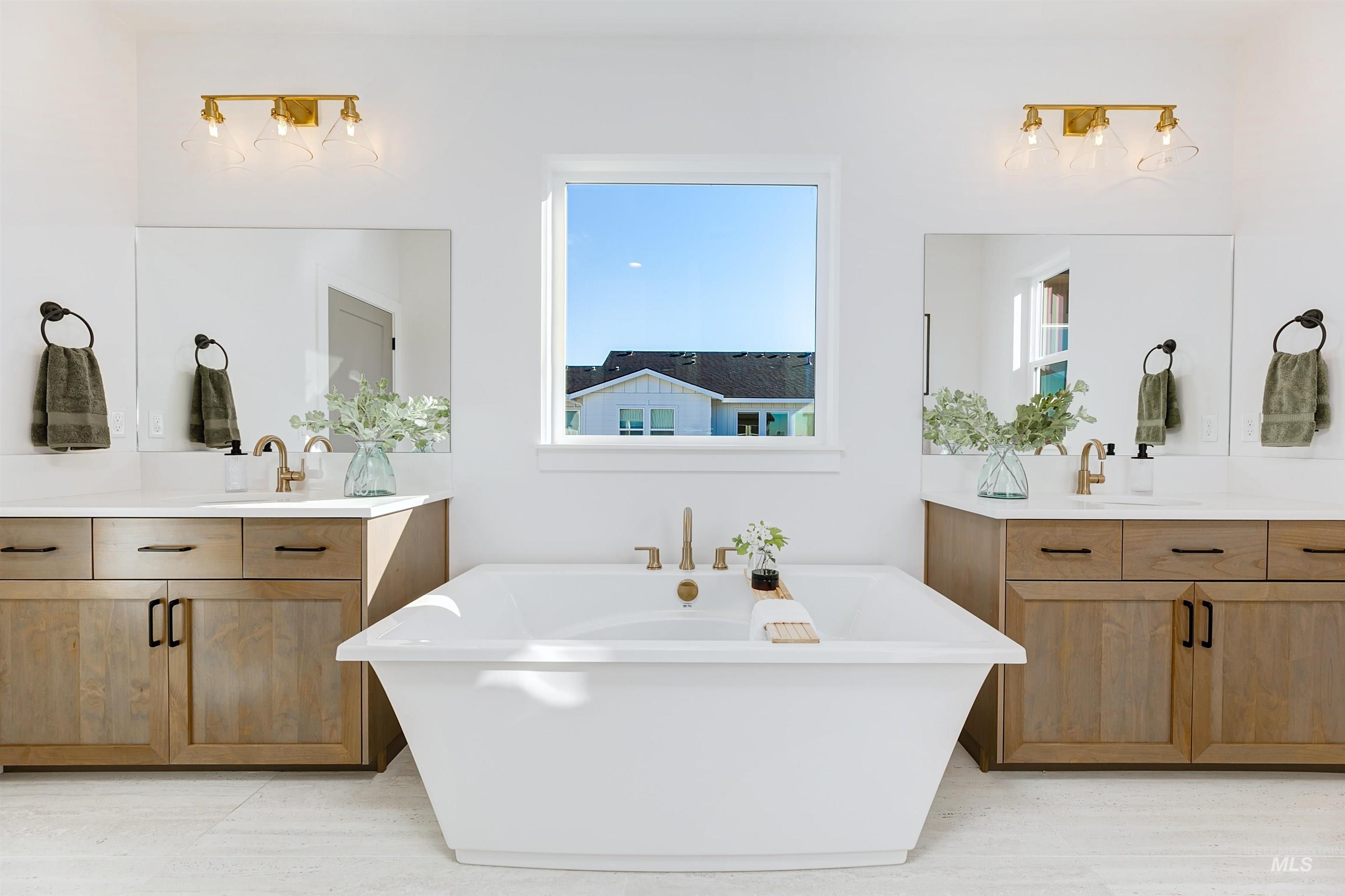Freestanding soaking tub centered under a window, flanked by dual wood-finish vanities with undermount sinks and light-toned countertops