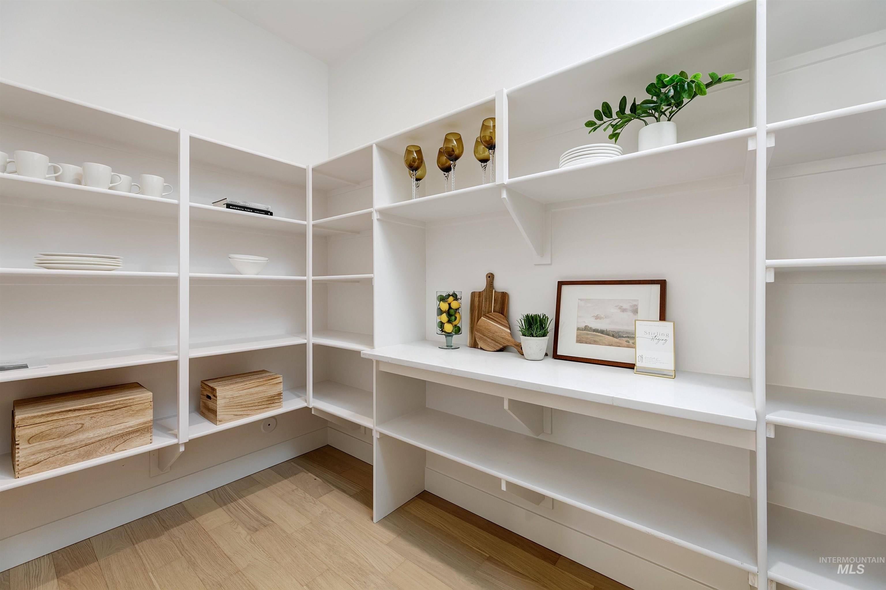 Custom pantry featuring abundant white shelving, integrated countertop space, and wood-finish flooring