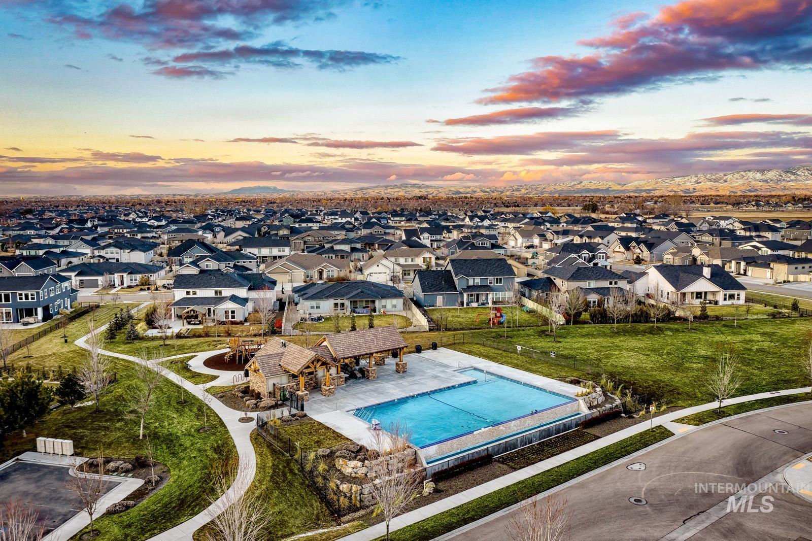 Community pool with a stone-clad pavilion, surrounding green spaces, paved pathways, and a backdrop of residential homes