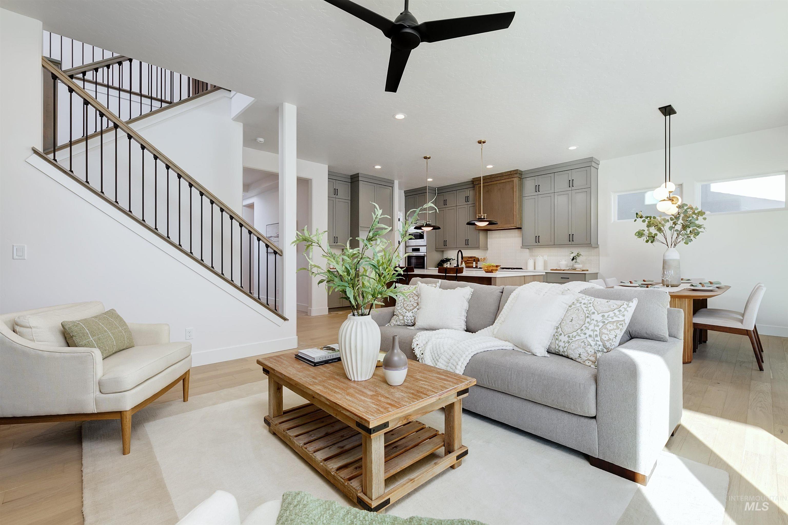 Open-concept living space featuring light wood-finish flooring, a modern black ceiling fan, and a staircase with dark metal balusters and wood handrails