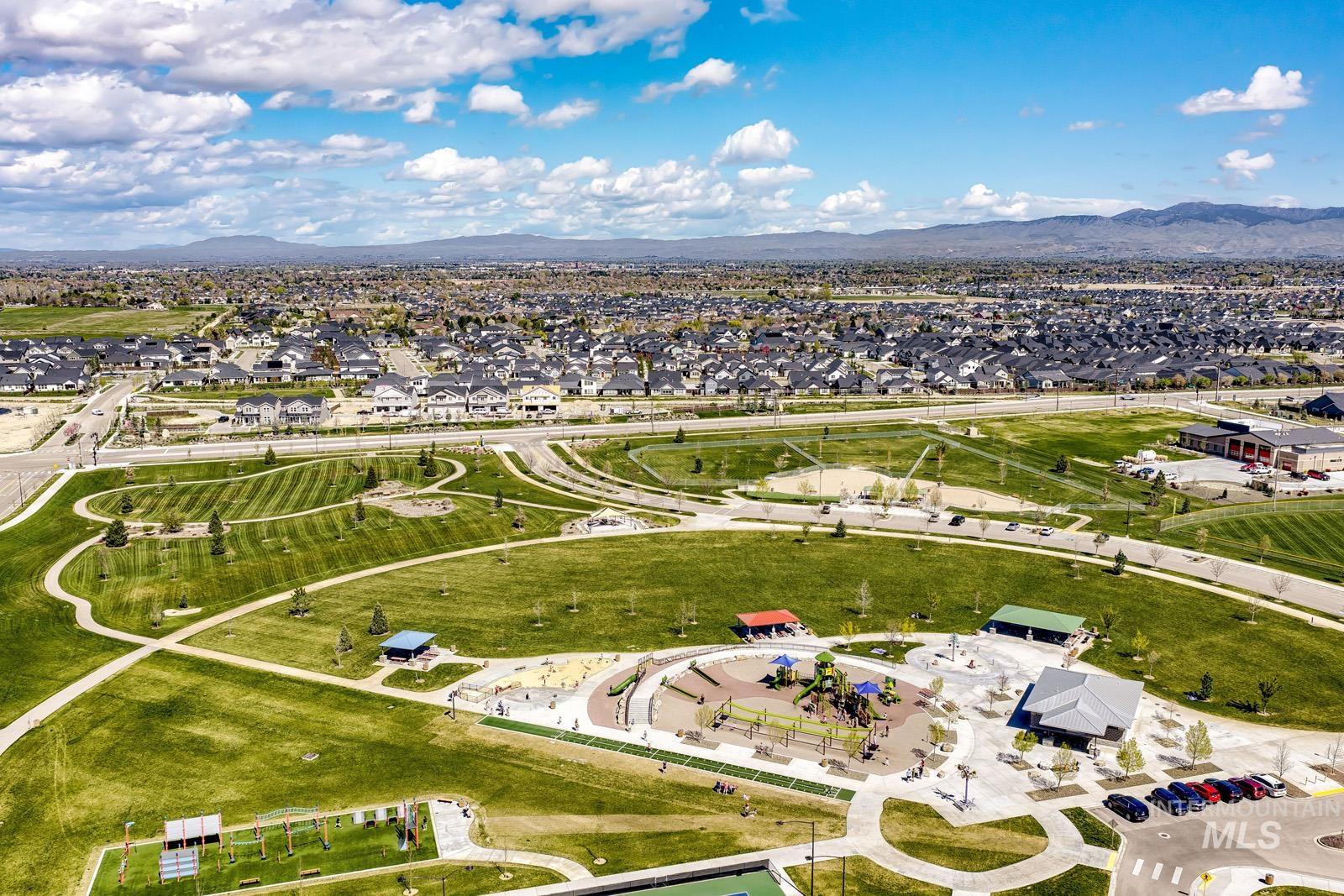 Expansive community park featuring a playground area, multiple sports fields, paved walking paths, shaded picnic structures, and manicured green spaces