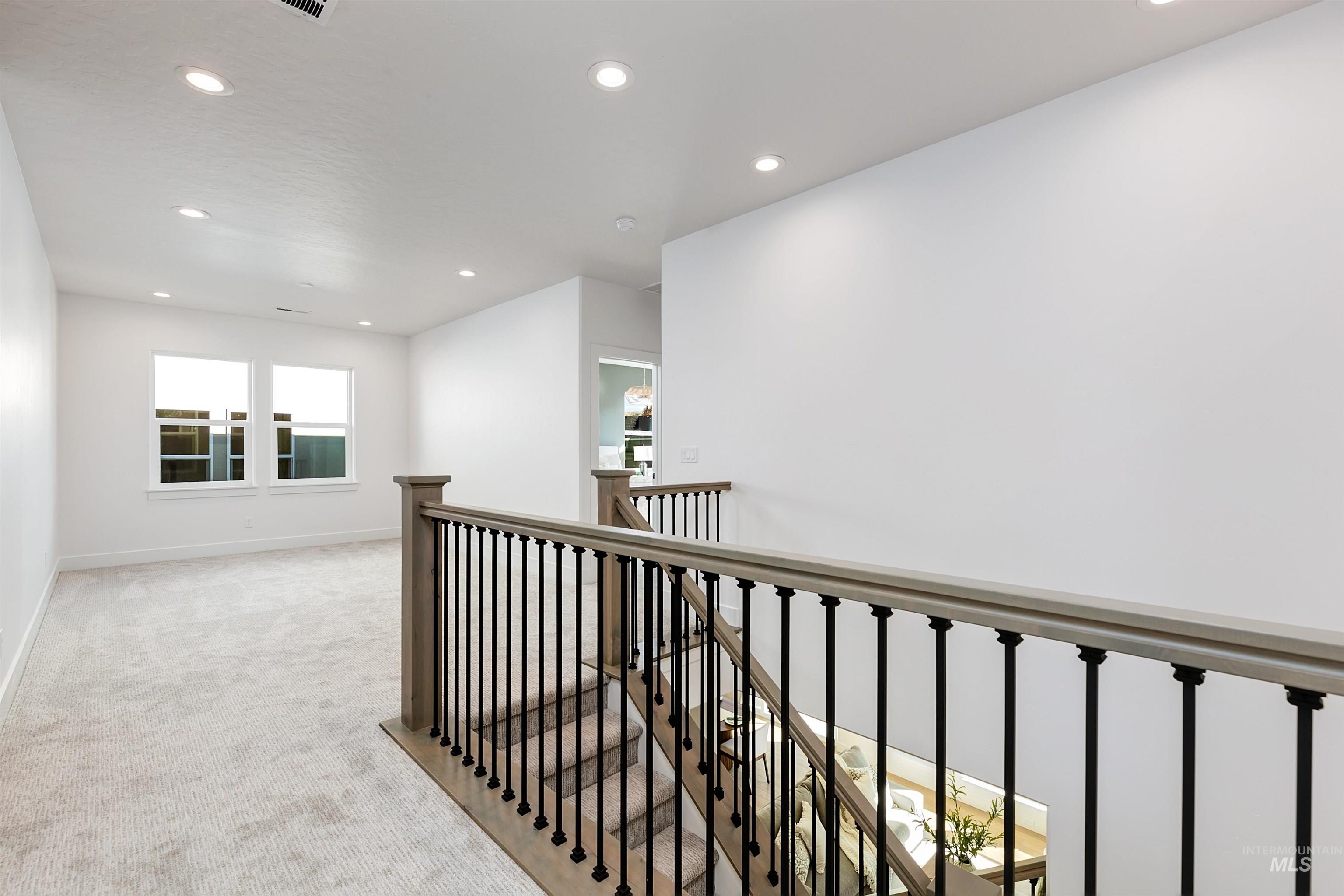 Staircase with wood handrail, black wrought iron balusters, and carpeted treads