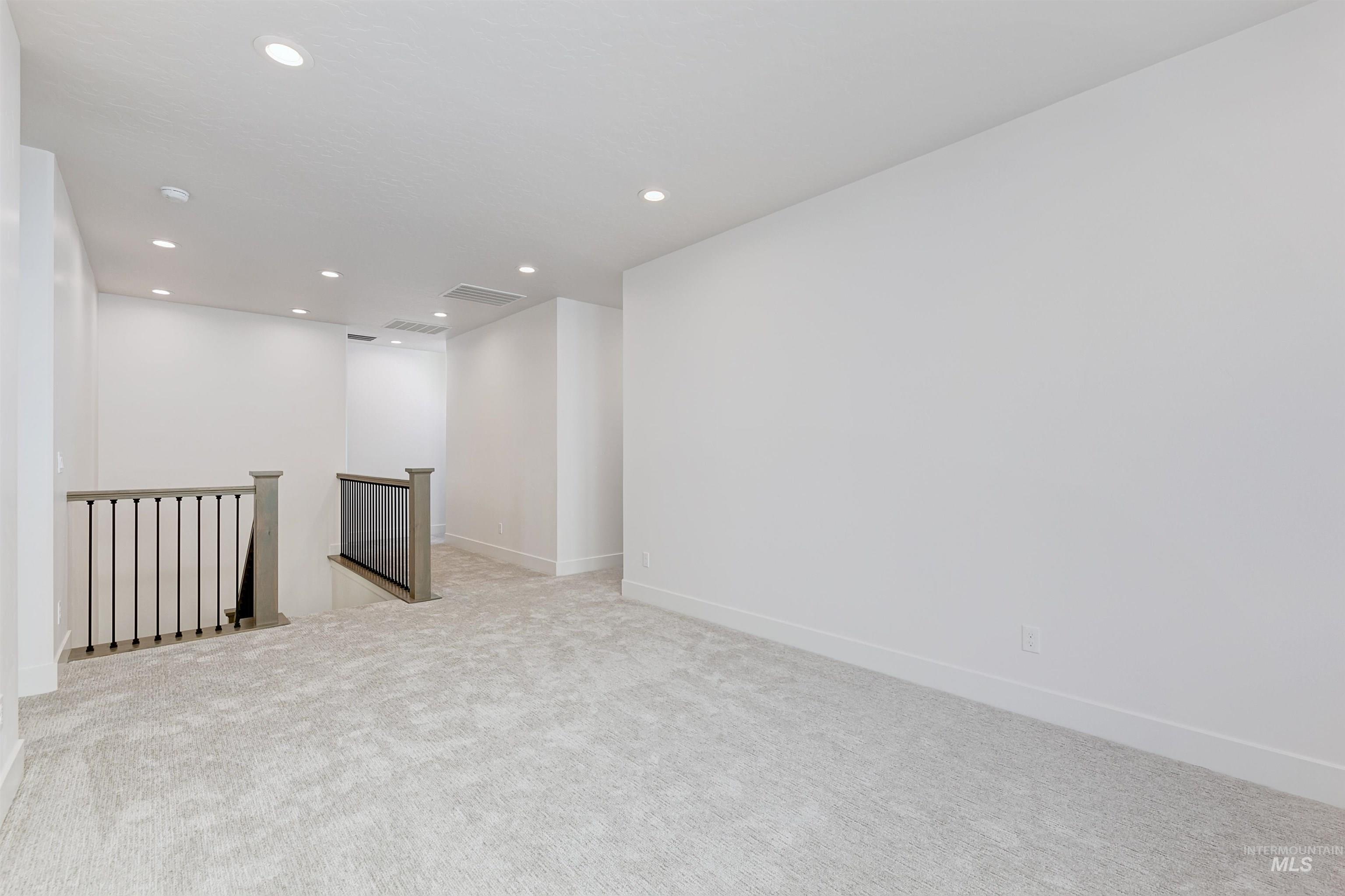 Open concept loft space featuring light-toned carpeting, recessed lighting, white walls, and contemporary gray newel posts with black metal balusters