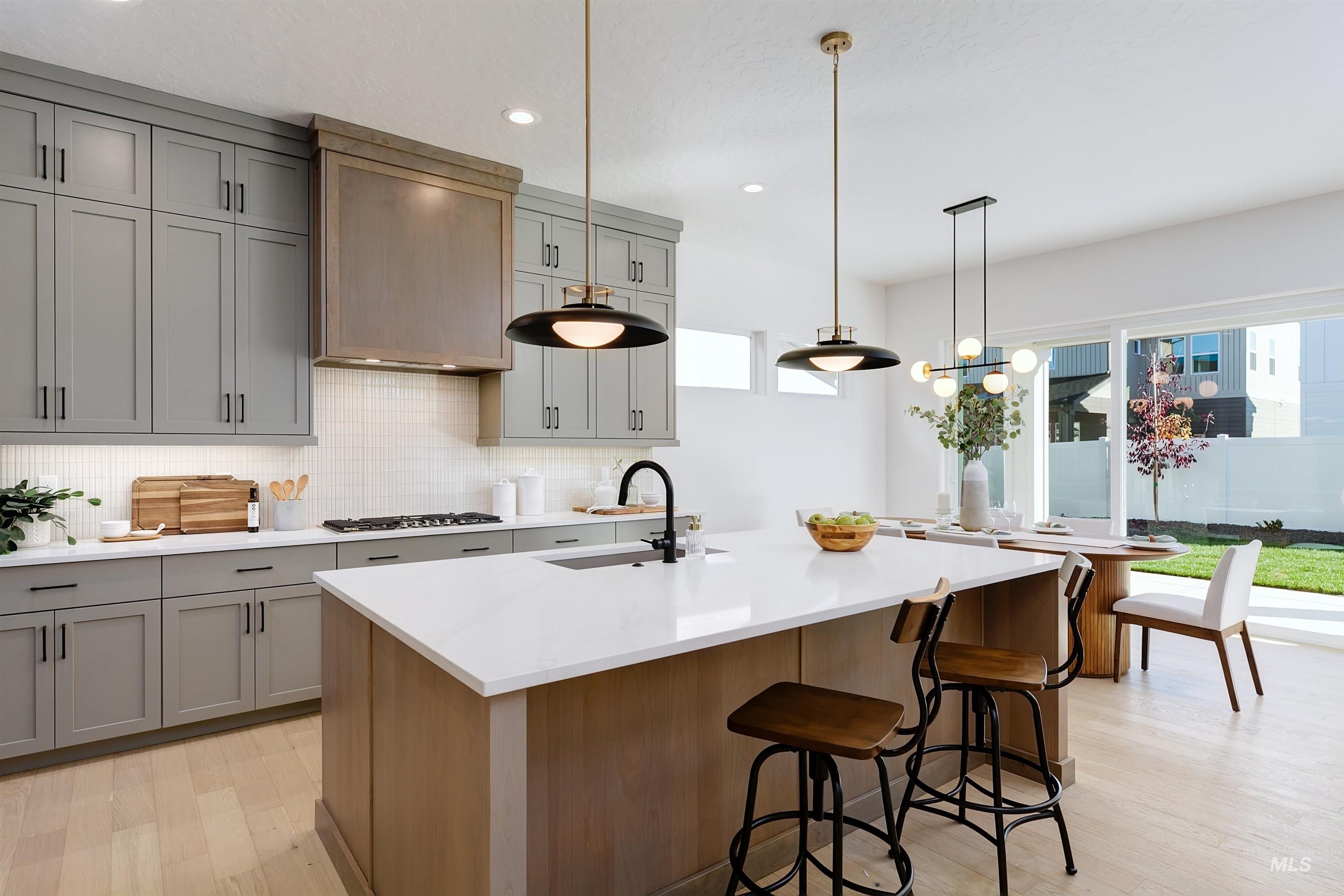 Open-concept kitchen featuring an expansive island with a white solid surface countertop, light wood-finish cabinetry, gray shaker-style perimeter cabinets, and a white subway tile backsplash