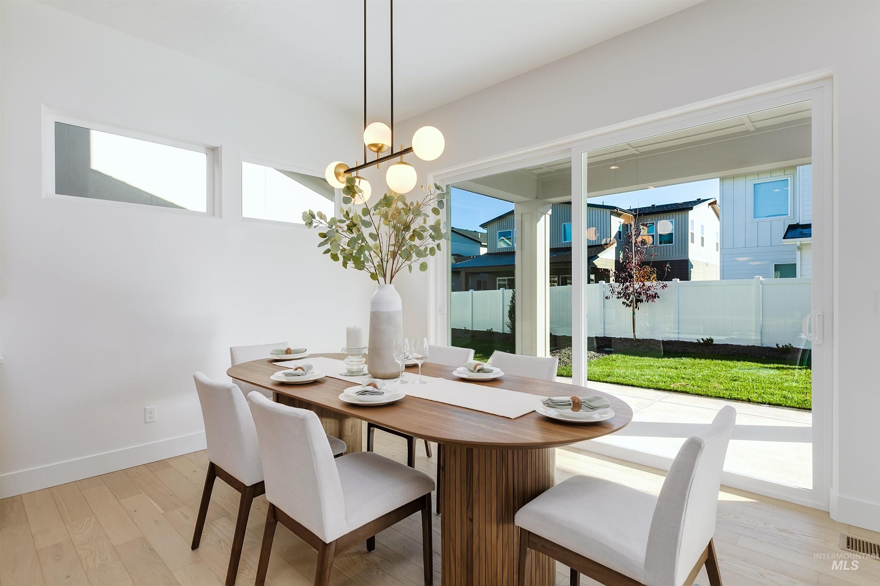 Dining area featuring wood-finish flooring, a contemporary chandelier, high windows, and a sliding glass door providing access to the backyard with a concrete patio