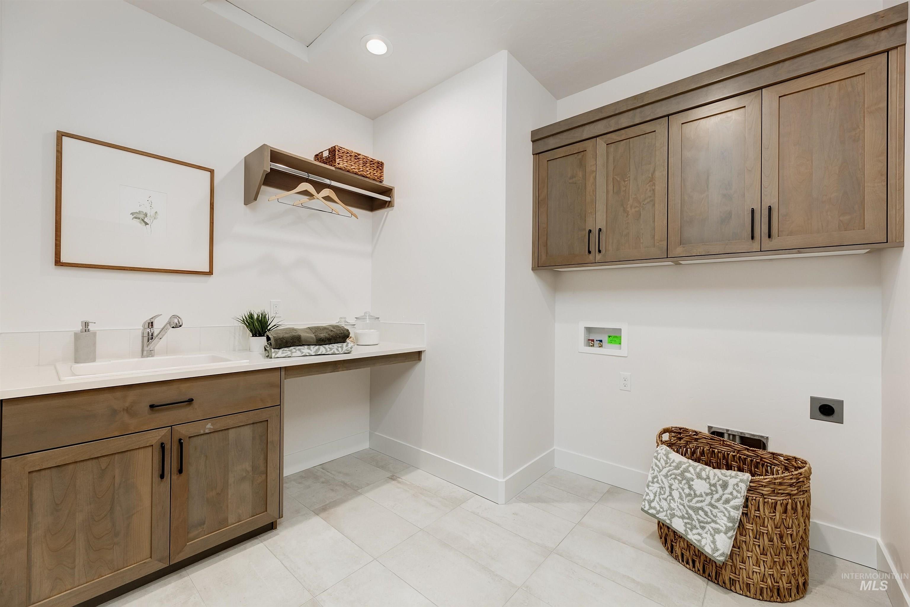 Laundry room featuring light wood-finish cabinetry, a single basin sink with a chrome faucet, white countertops, recessed lighting, and light tile flooring