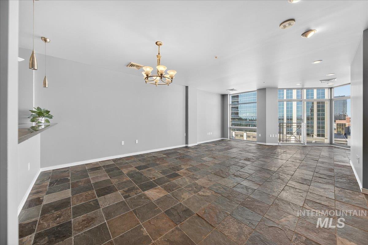 Unfurnished living room with stone tile flooring, a chandelier, a wall of windows, and recessed lighting