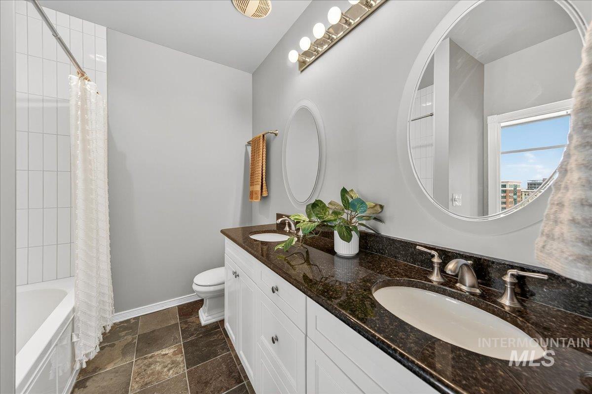 Full bathroom featuring shower / tub combo, double vanity, and dark stone finish floors