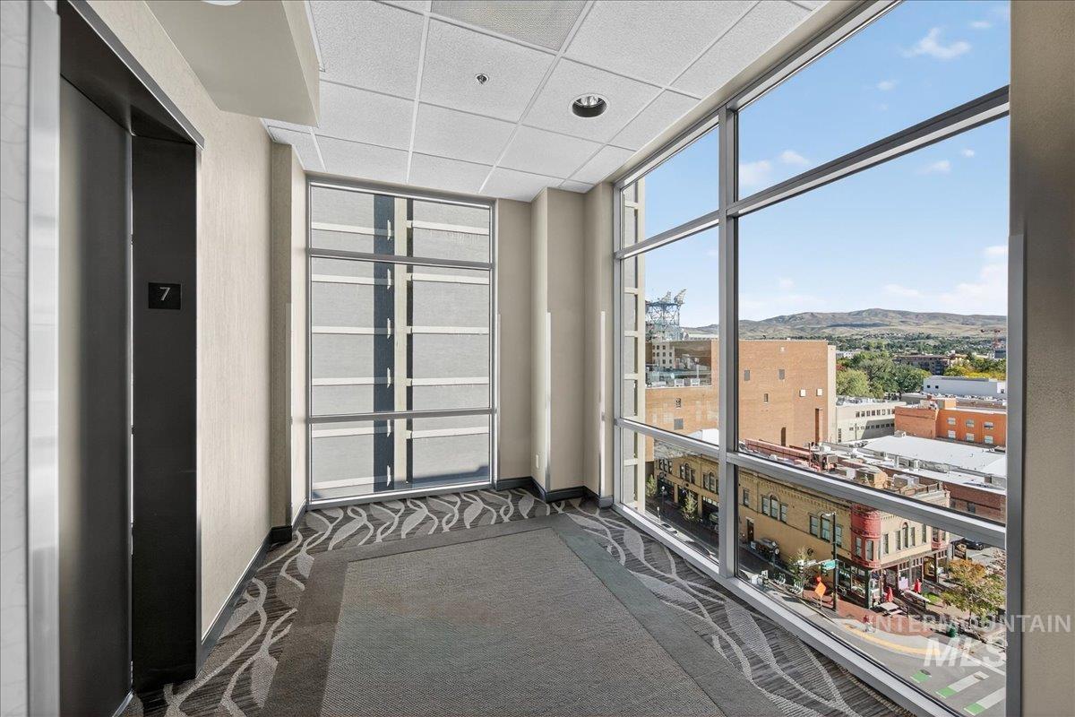 Hall with expansive windows, elevator, a drop ceiling, dark colored carpet, and a mountain view