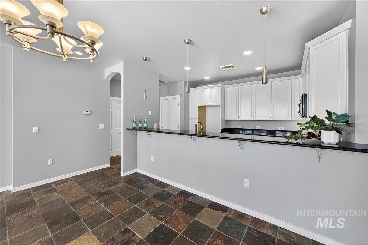 Kitchen with stone tile floors, arched walkways, pendant lighting, white cabinetry, and recessed lighting