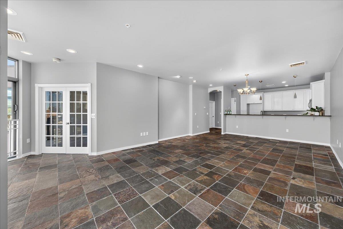 Unfurnished living room featuring stone tile floors, arched walkways, recessed lighting, french doors, and a chandelier