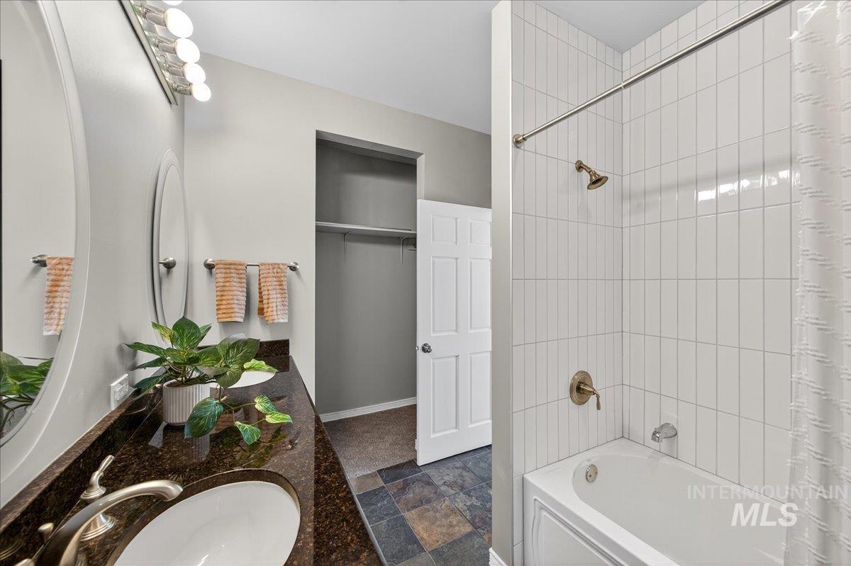 Full bathroom with shower / tub combo, double vanity, and dark stone finish floors
