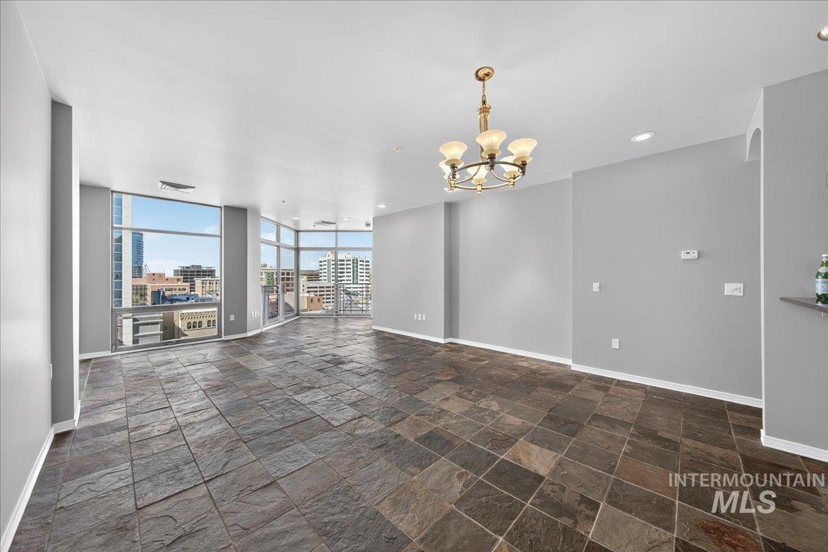 Unfurnished living room featuring stone tile floors, a view of city, a chandelier, expansive windows, and recessed lighting