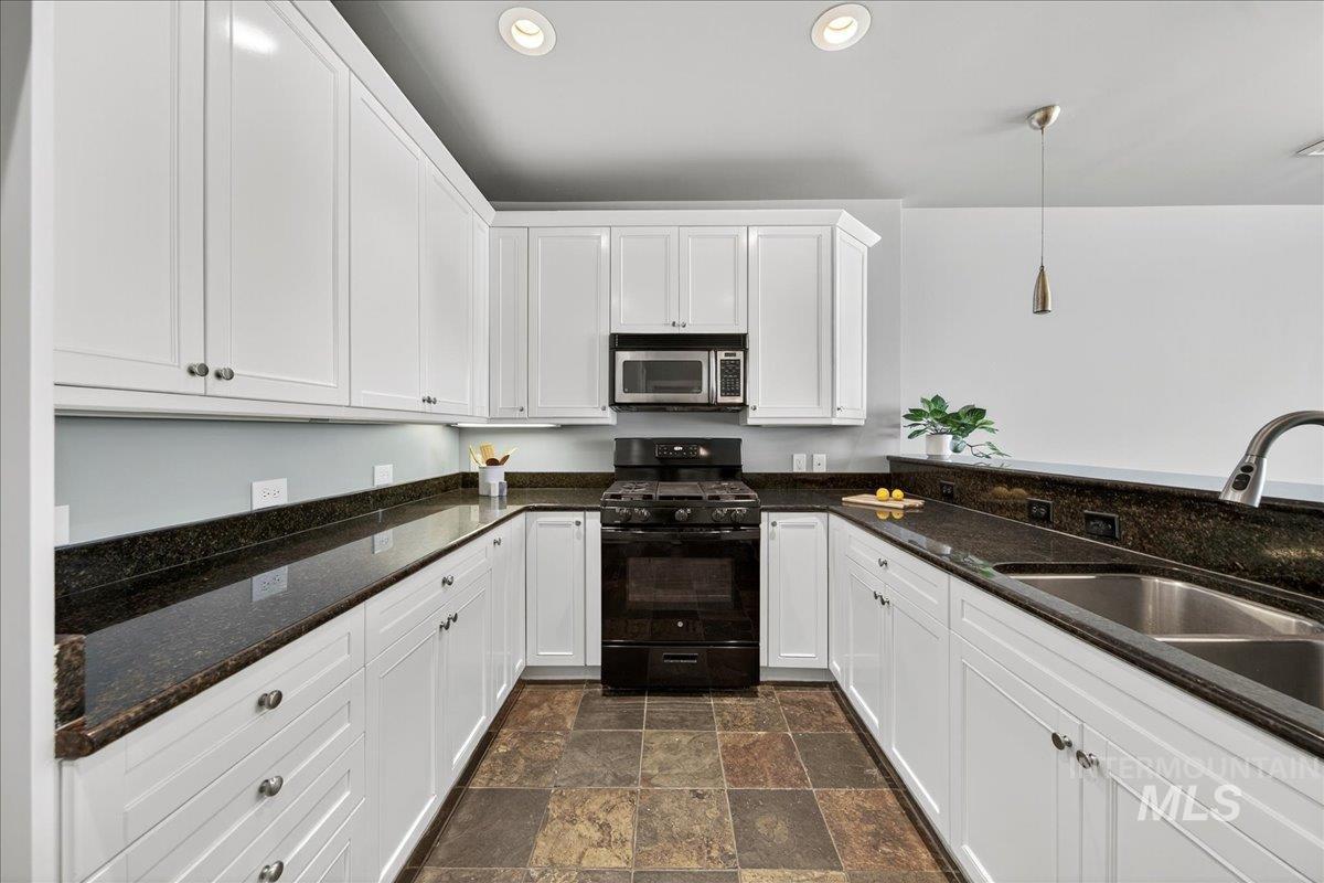 Kitchen featuring black gas range oven, white cabinetry, pendant lighting, dark stone countertops, and stainless steel microwave