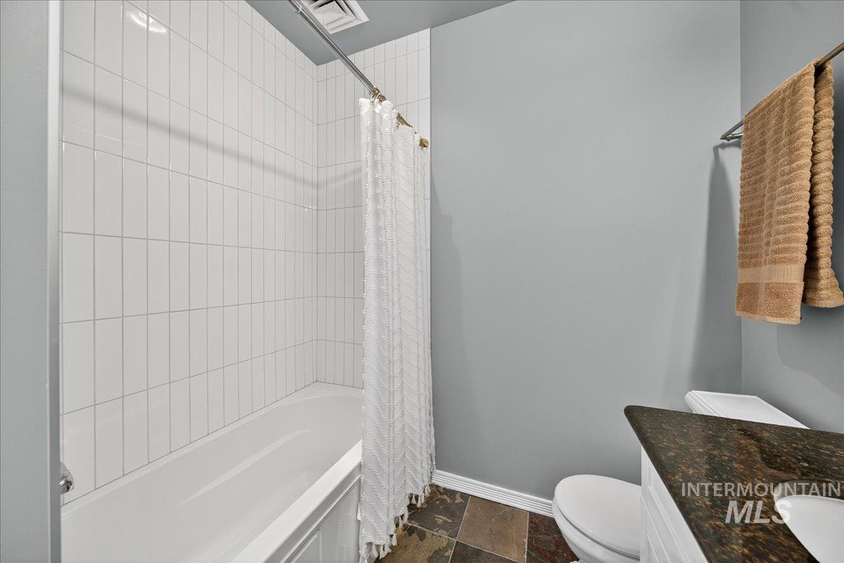 Full bathroom with shower / bath combination with curtain, vanity, and dark stone finish flooring