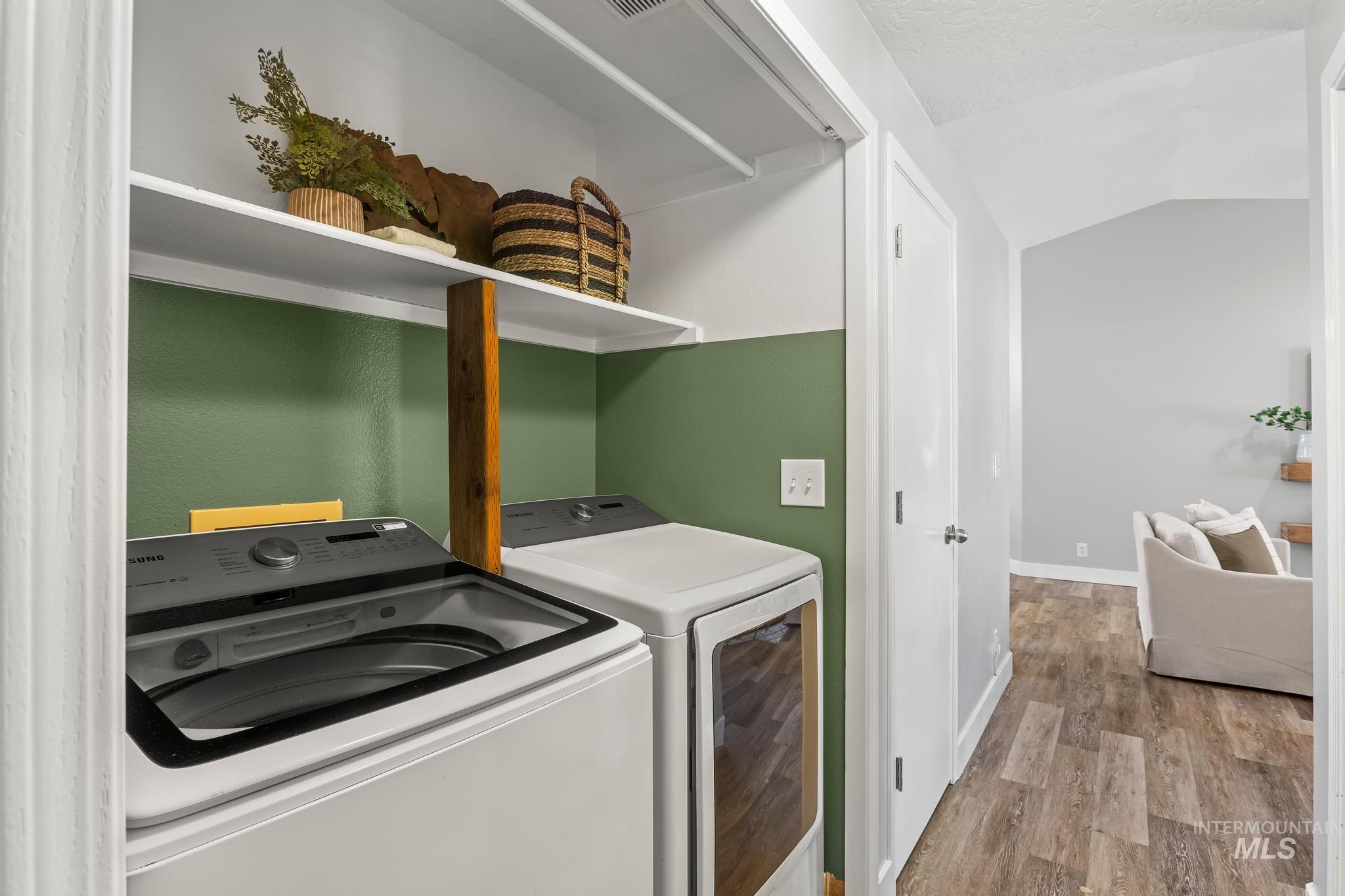Laundry area with light wood-style flooring, lofted ceiling, independent washer and dryer, and a textured ceiling