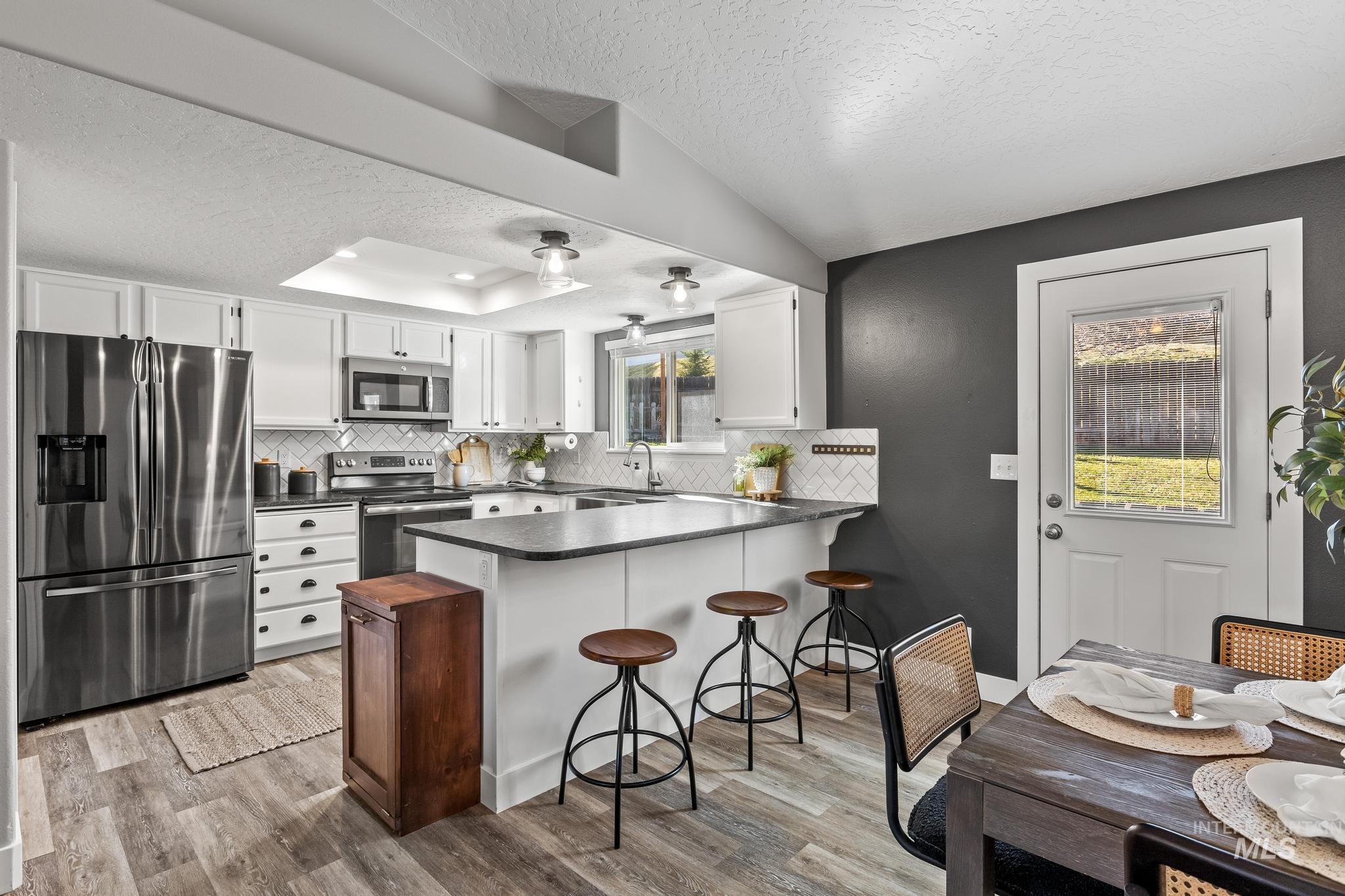 Kitchen with a textured ceiling, appliances with stainless steel finishes, white cabinets, a peninsula, and a kitchen breakfast bar