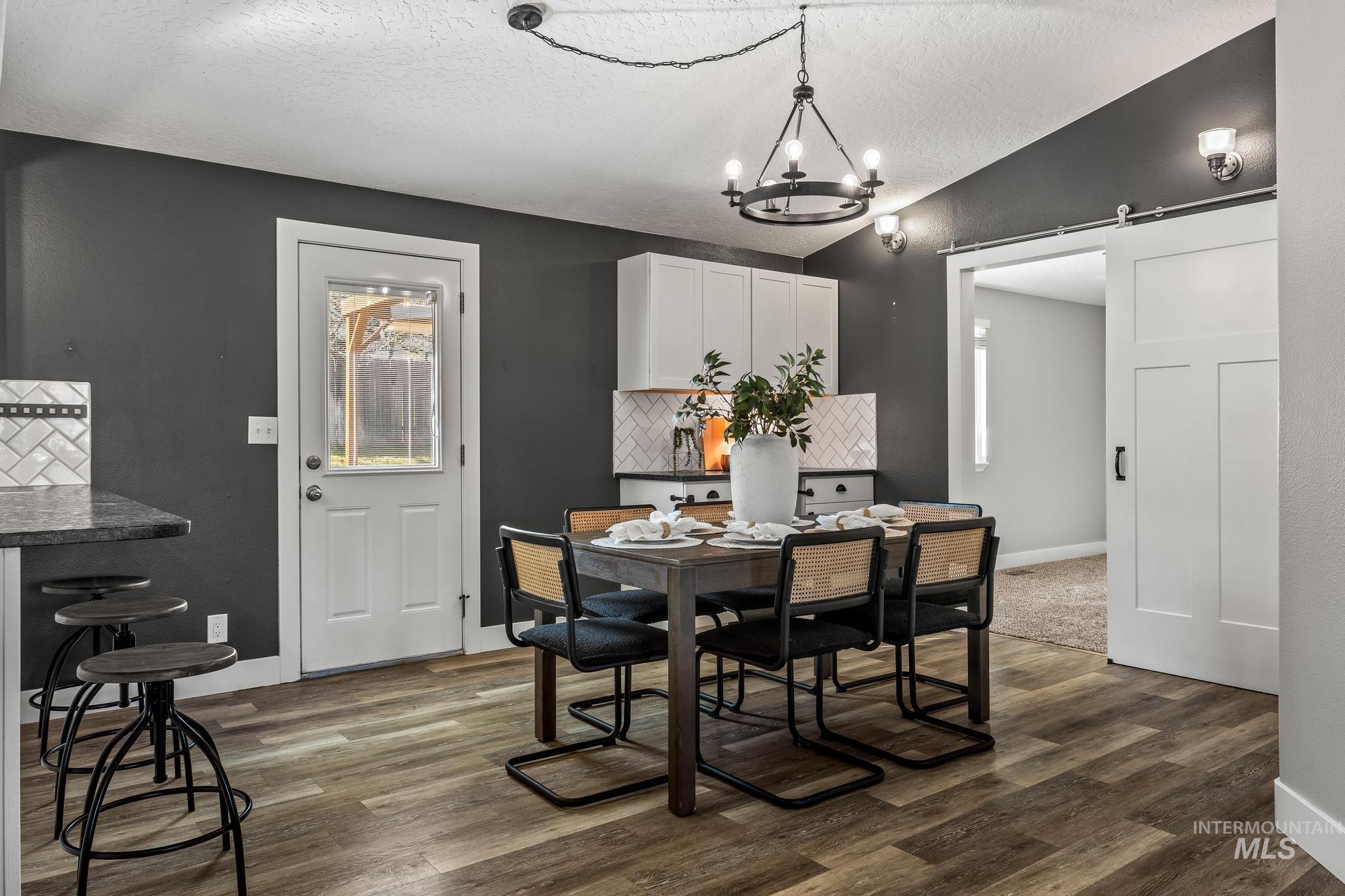 Dining room with a barn door, a textured ceiling, dark wood-style flooring, vaulted ceiling, and a chandelier
