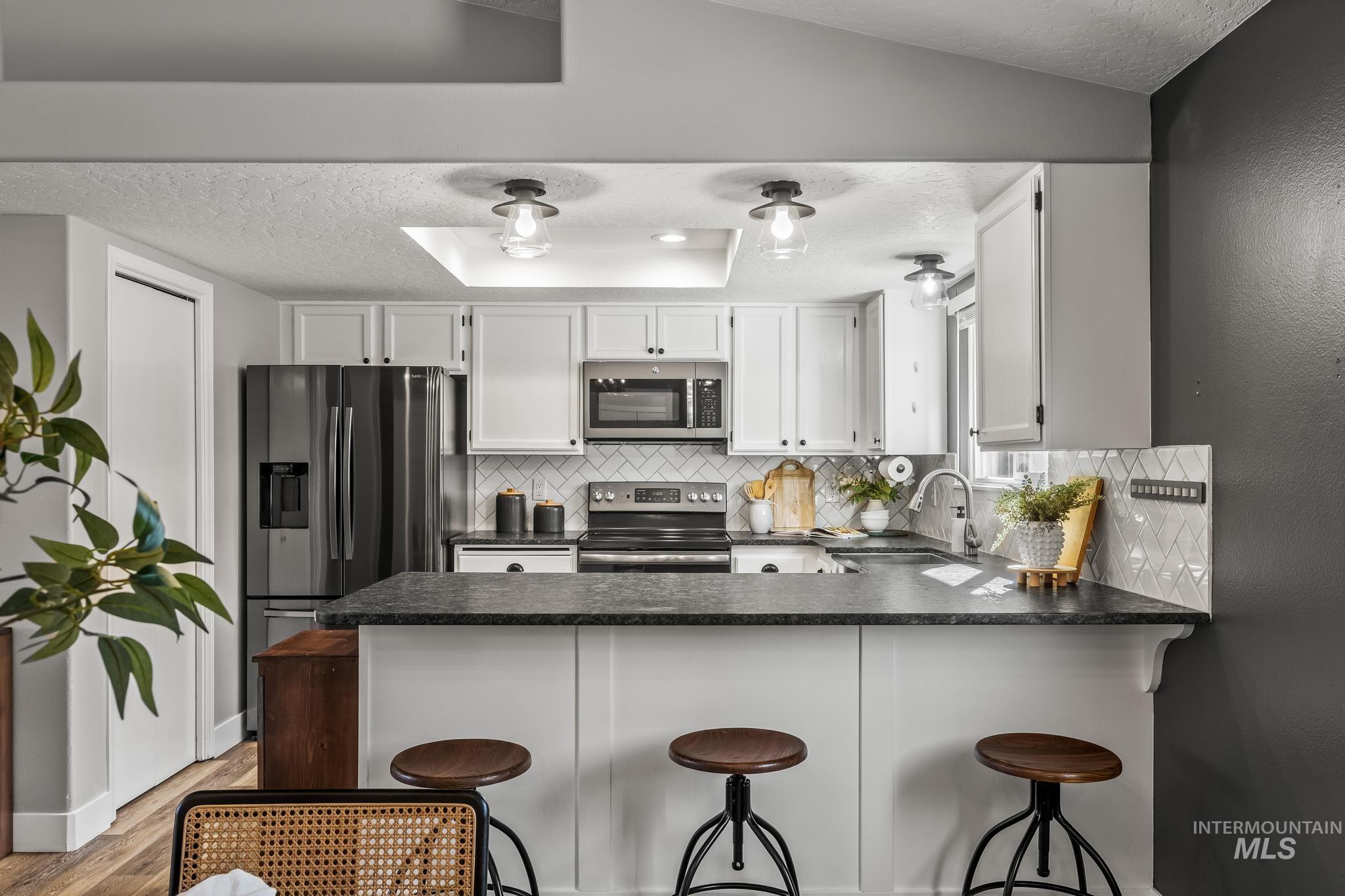 Kitchen with dark countertops, a textured ceiling, white cabinets, appliances with stainless steel finishes, and a kitchen bar
