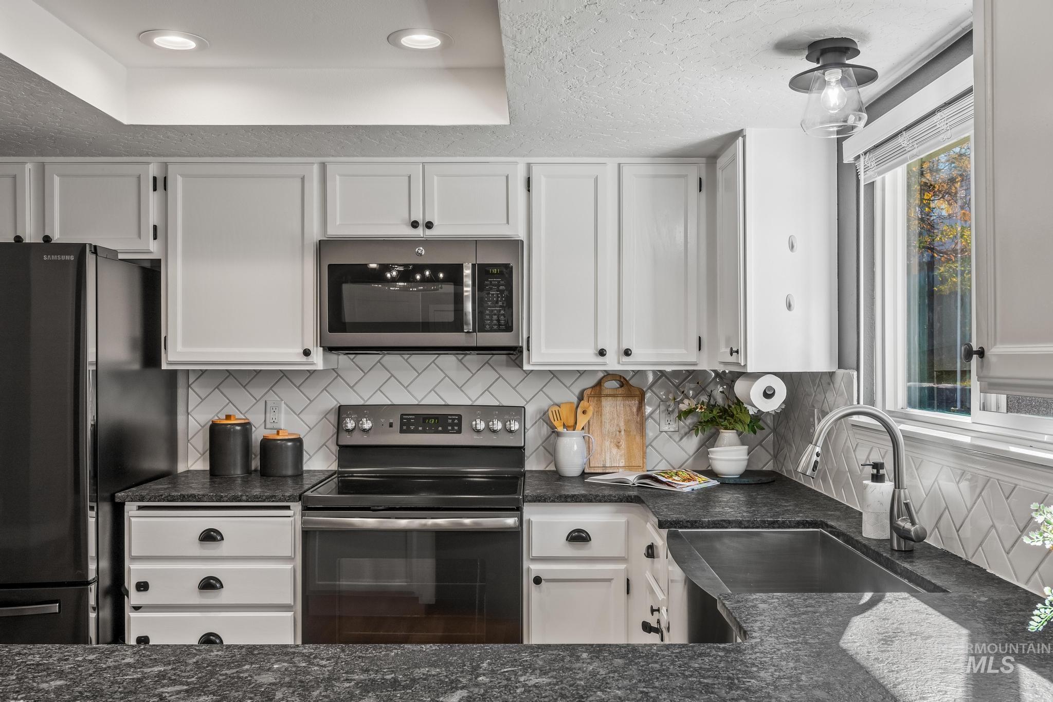 Kitchen with backsplash, stainless steel appliances, white cabinetry, recessed lighting, and dark stone counters