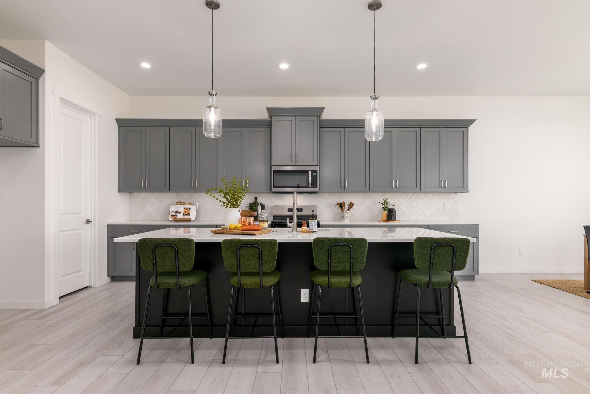Kitchen featuring a breakfast bar, gray cabinets, decorative backsplash, a kitchen island with sink, and light wood-type flooring