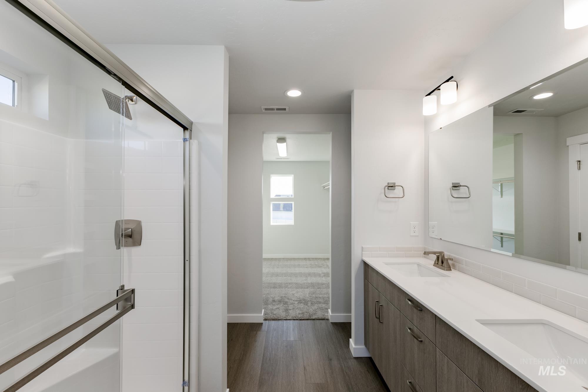 Full bath featuring dark wood-type flooring, a stall shower, double vanity, recessed lighting, and a closet