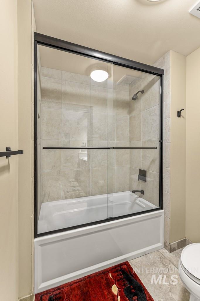 Full bath featuring toilet and shower / bath combination with glass door