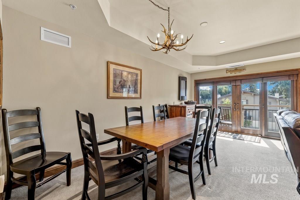 Dining room with a raised ceiling, light carpet, recessed lighting, and a chandelier
