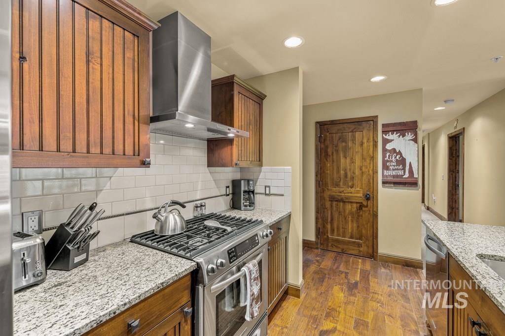 Kitchen with stainless steel appliances, wall chimney exhaust hood, light stone counters, dark wood finished floors, and recessed lighting