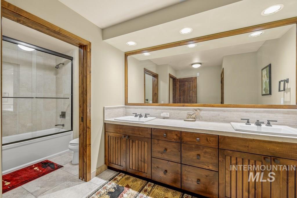 Bathroom with enclosed tub / shower combo, tasteful backsplash, double vanity, recessed lighting, and light tile patterned flooring