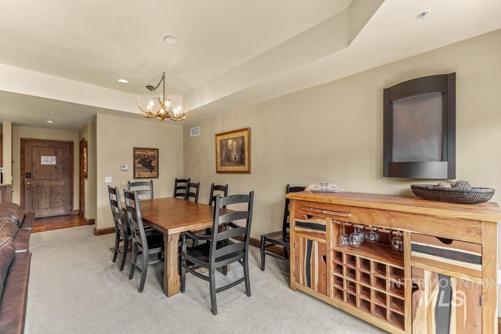 Dining room with light colored carpet, a chandelier, and a raised ceiling