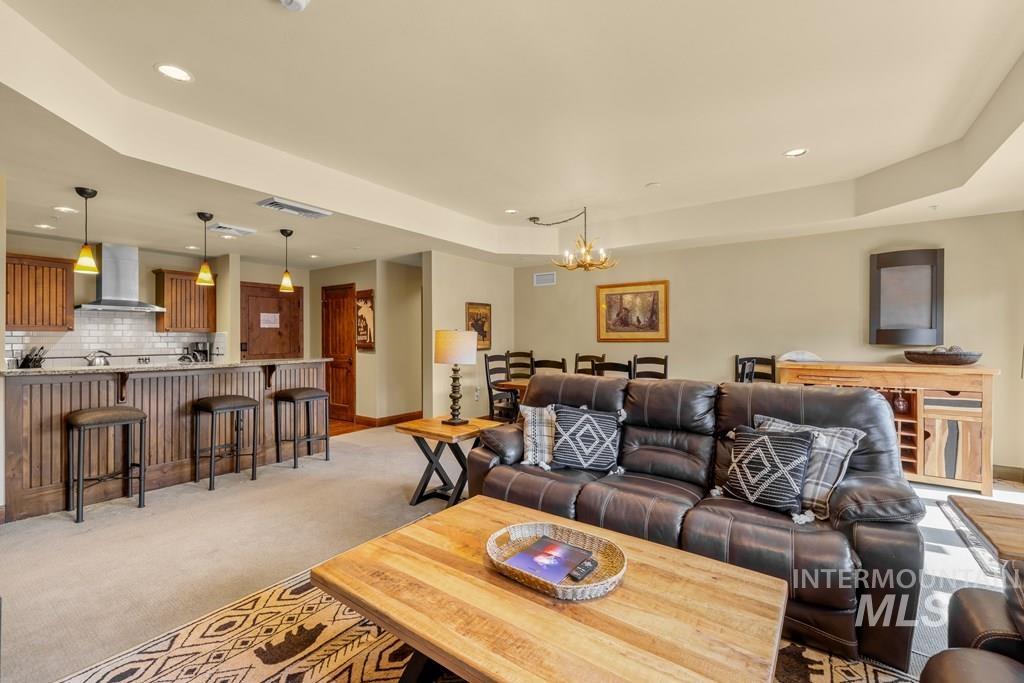 Living area with a tray ceiling, light colored carpet, recessed lighting, and a chandelier