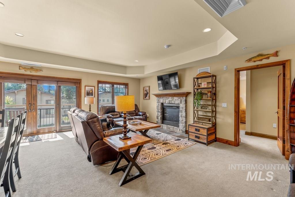 Living area featuring french doors, light colored carpet, a stone fireplace, recessed lighting, and a raised ceiling