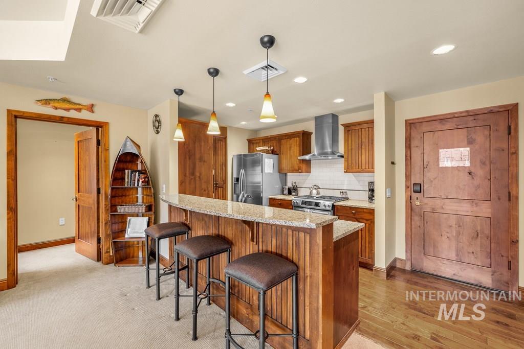 Kitchen featuring tasteful backsplash, light stone counters, hanging light fixtures, brown cabinetry, and recessed lighting