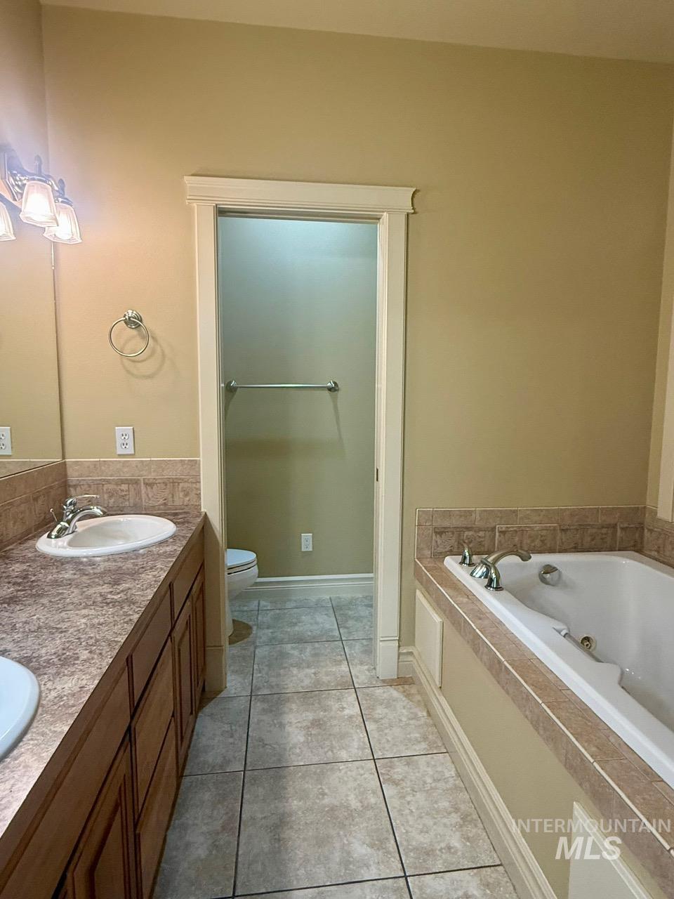 Bathroom with double vanity, a tub with jets, and light tile patterned flooring