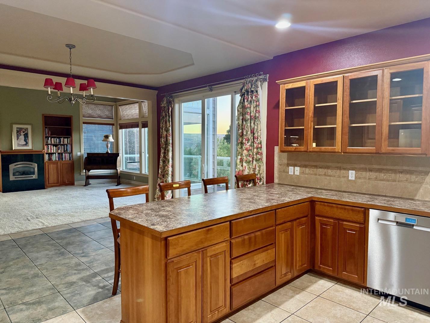 Kitchen featuring glass insert cabinets, wood finish cabinetry, a breakfast bar area, hanging lights, and dishwasher