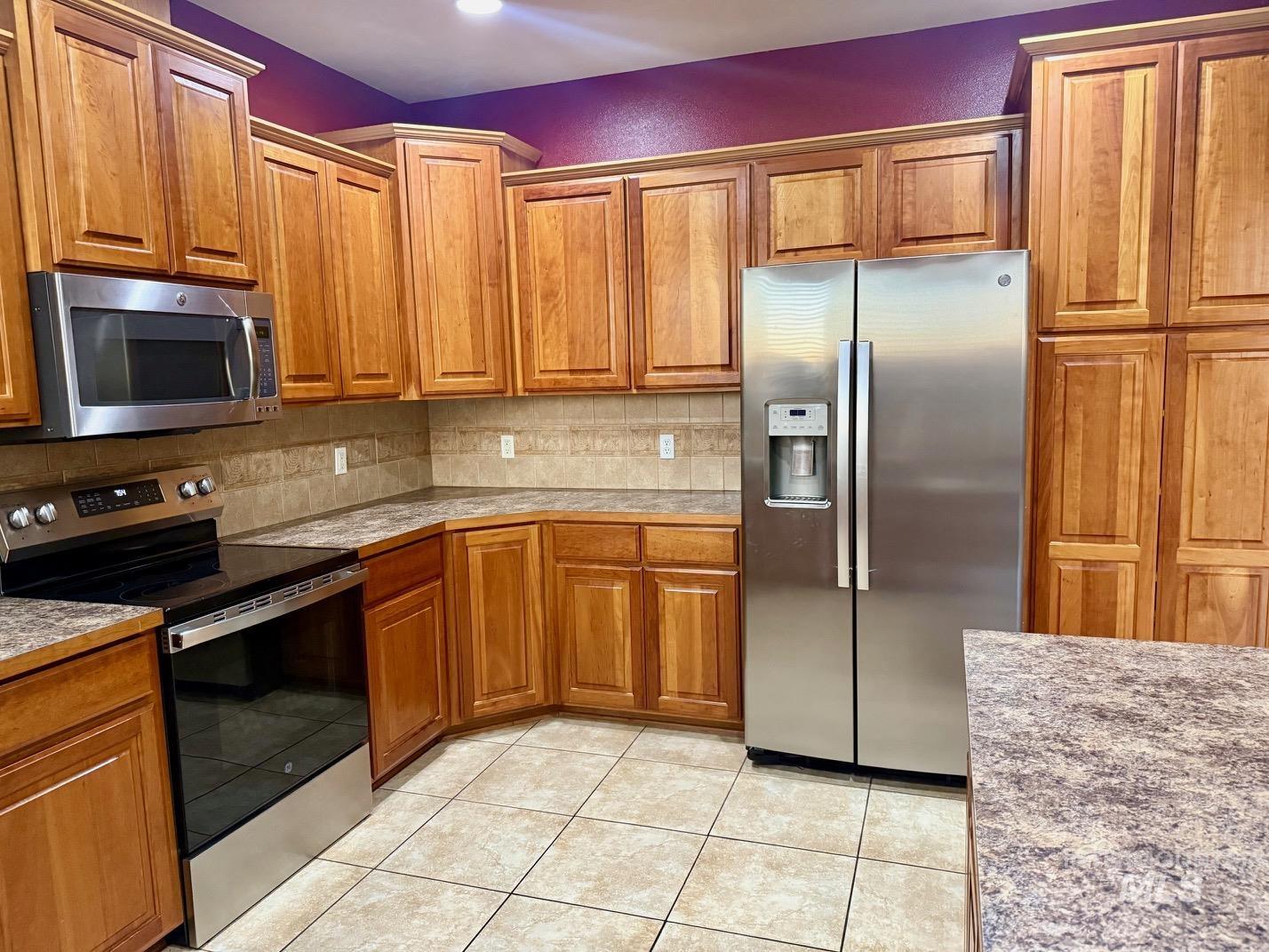 Kitchen with stainless steel appliances, wood finish cabinetry, light countertops, and light tile patterned flooring