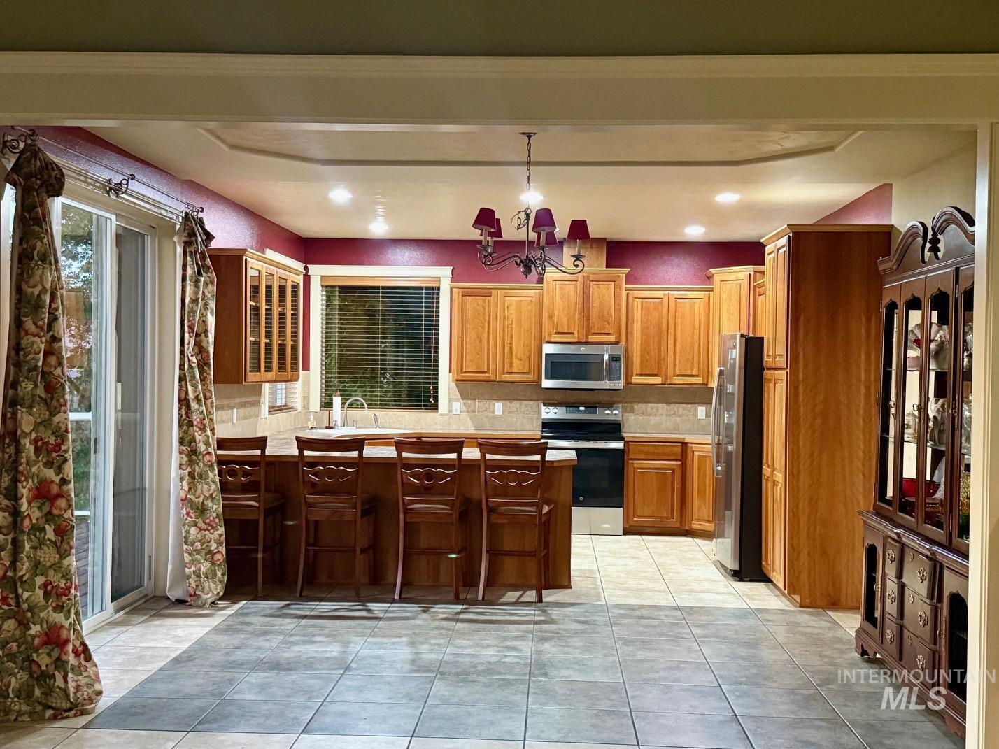 Kitchen with stainless steel appliances, light countertops, light tile patterned flooring, a peninsula, and a breakfast bar area