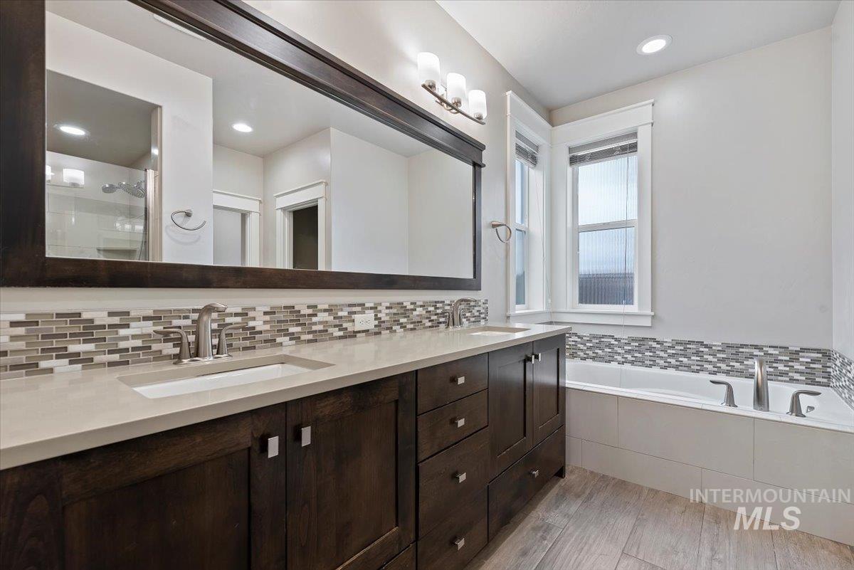 Full bath with double vanity, a bath, light wood finished floors, recessed lighting, and a shower