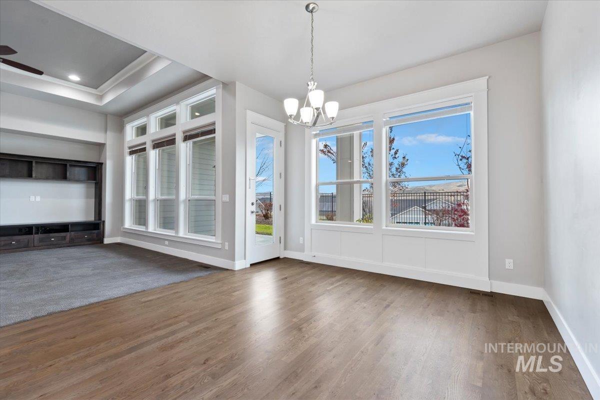 Unfurnished dining area with wood finished floors, a chandelier, a raised ceiling, a ceiling fan, and recessed lighting