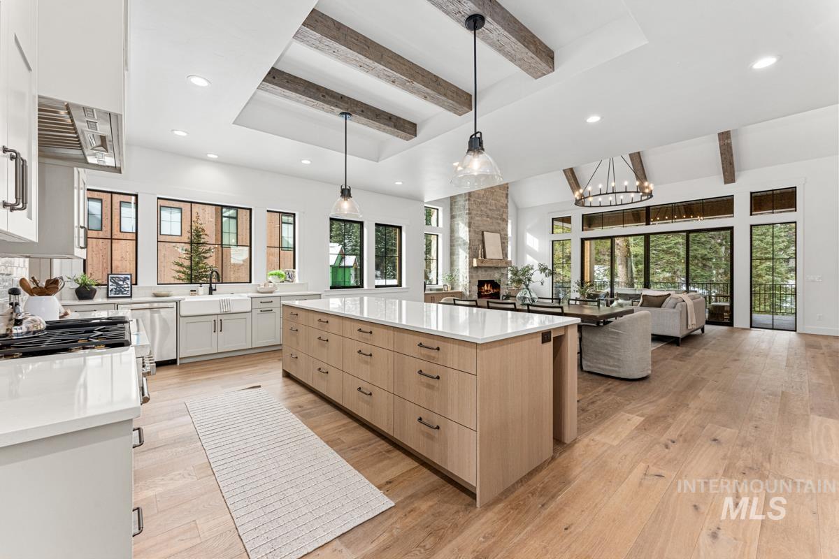 Dual tone kitchen featuring beamed ceiling, a kitchen island, light stone counters, suspended lighting, and two tone cabinets