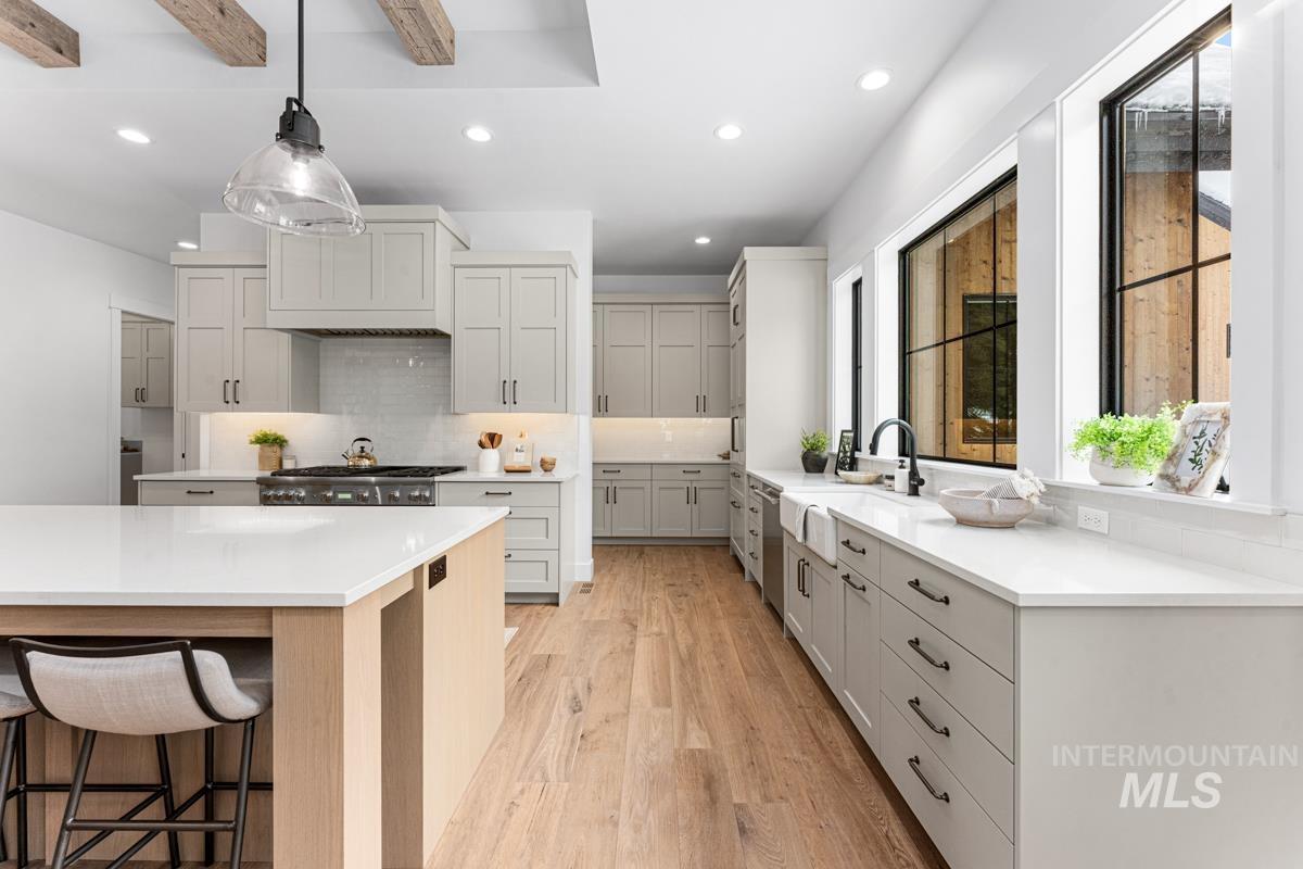 Kitchen with backsplash, light wood-type flooring, a breakfast bar area, decorative light fixtures, and light stone countertops