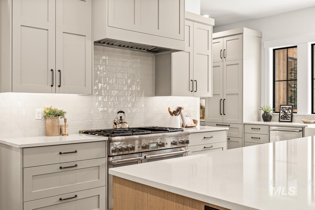 Kitchen featuring decorative backsplash, light stone counters, stainless steel appliances, and white cabinetry