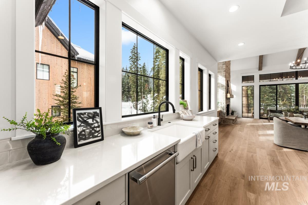 Kitchen with stainless steel dishwasher, light wood finished floors, suspended lighting, healthy amount of natural light, and beamed ceiling
