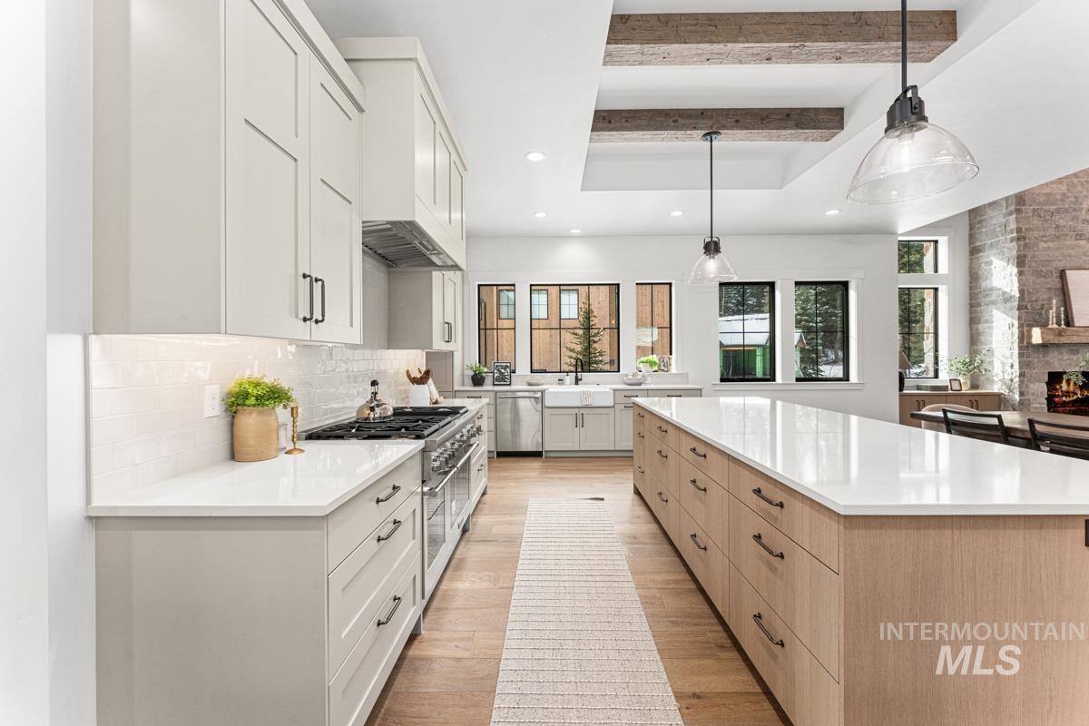 Two tone kitchen featuring beamed ceiling, two tone color scheme, stainless steel appliances, light stone countertops, and a spacious island