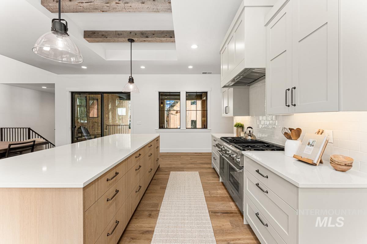 Kitchen with range with two ovens, dual tone cabinetry, light wood-type flooring, a spacious island, and a tray ceiling