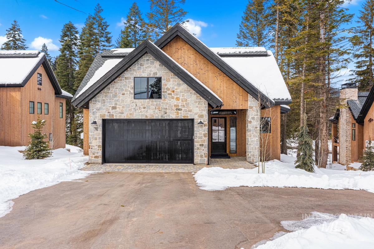 View of front of property featuring stone siding, a garage, and driveway